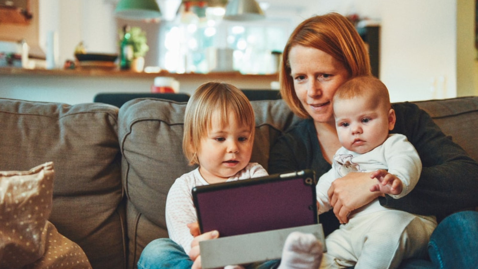 A mom holding her young children while using a tablet