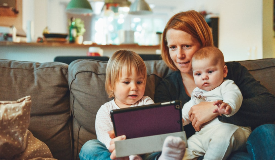 A mom holding her young children while using a tablet custody